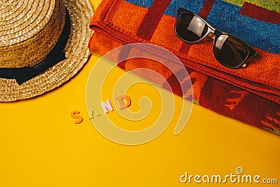 Concept of relaxing on the beach. inscription sand on a yellow background with sunglasses, a towel and a straw hat. top view Stock Photo