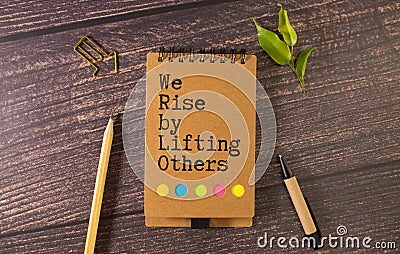 Concept of We Rise By Lifting Others write on paperwork isolated on Wooden Table. Stock Photo