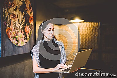 The concept of small business and technology. Young beautiful brunette businesswoman in black dress and gray sweater stands in Stock Photo