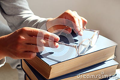 The concept of spending time reading books by elderly people. Reading glasses in hands on a stack of books, gray background, space Stock Photo