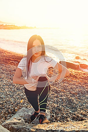 The concept of sport. A young brunette woman is engaged in stretching on the coastal rocks. At the back of the sea. Top view of Stock Photo