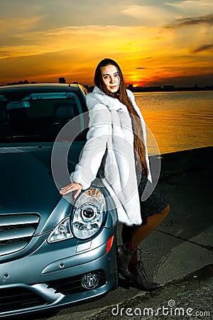 Strong independent young woman with car. Beautiful serious girl fashionably stand near vehicle at sunset Stock Photo