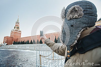 Concept of travel. The tourist in a cap makes photos on his phone Moscow landscape with the Kremlin Intercession Cathedral on Red Stock Photo