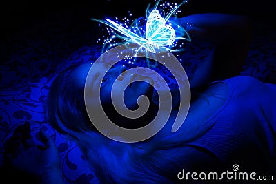 Concept of a woman laying in bed in the dark, illuminated with blue light from floating magical butterfly Stock Photo