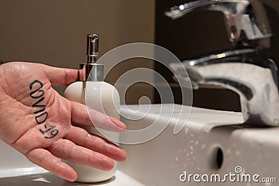 Conceptual close up shot of the left hand of a Caucasian man. On the palm there is the word covid-19, immediately next to the sink Stock Photo