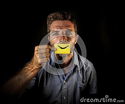 Conceptual dramatic portrait of young depressed man holding paper with happy smiley mouth draw on his lips looking miserable and f Stock Photo