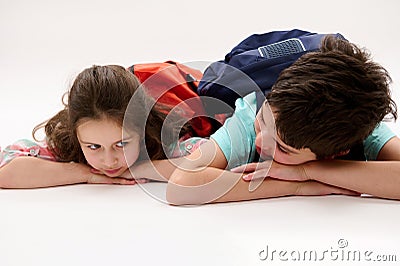 Happy little preschool girl and her brother, teen school boy with backpacks lying on belly, isolated on white background Stock Photo