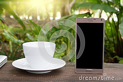 Conceptual green workspace, mobile with blank screen on table, coffee cup and green garden background, business technology conce Stock Photo