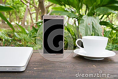 Conceptual green workspace, mobile with blank screen on table, coffee cup and green garden background, business technology conce Stock Photo