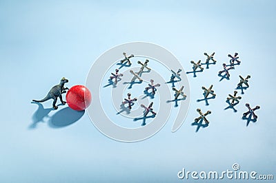 Conceptual photo of dinosaur rolling a red ball toward antique jacks. Stock Photo