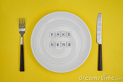 Conceptual photo, table setting with an empty plate, fake news consumption by the public or consumers- `Fake news` on yellow backg Stock Photo
