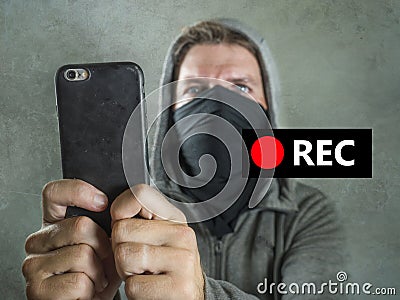 Conceptual portrait of young rioter filming street chaos . ultra and radical man masked recording riot video on mobile phone Stock Photo