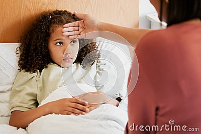Concerned, anxious and unwell girl suffering with cold or flu while her mother checks her temperature at home. Worried Stock Photo