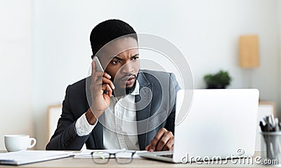 Concerned businessman talking on cellphone and looking at laptop screen Stock Photo