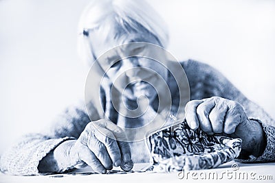 Concerned elderly woman sitting at the table counting money in her wallet. Black and white blue toned image. Stock Photo