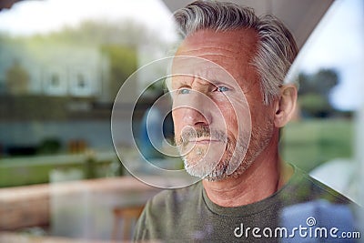 Concerned Senior Man Standing And Looking Out Of Kitchen Door Viewed Through Window Stock Photo