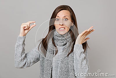 Concerned young woman in gray sweater, scarf spreading hands holding medication tablet, aspirin pill isolated on grey Stock Photo