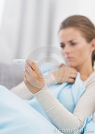 Concerned young woman looking on thermometer Stock Photo