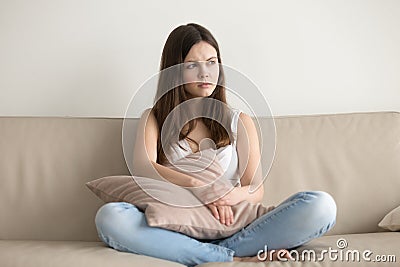 Concerned young woman sitting on sofa at home Stock Photo