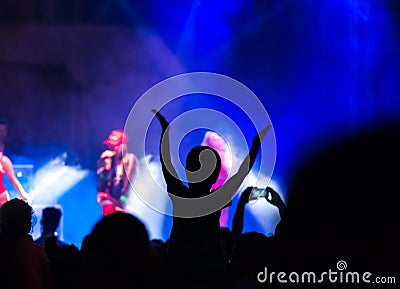 Concert crowd attending a concert, people silhouettes are visible, backlit by stage lights. Raised hands and smart phones are visi Stock Photo