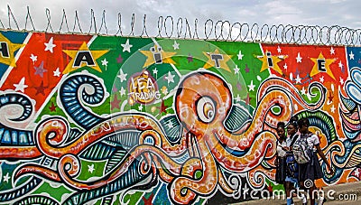 Concertina wire atop colorful mural serves as backdrop to school girls in Cap Haitien. Editorial Stock Photo