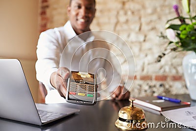 Concierge at hotel reception holds credit card reader to camera Stock Photo