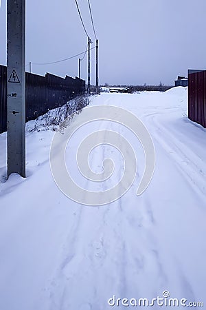 Concrete electric pillars on a rustic street next to a fence in winter and a snowy street Stock Photo