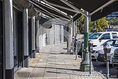 A concrete sidewalk lined with parked meters and parked cars and trucks with lush green palm trees and plants in Hollywood Editorial Stock Photo