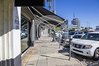 A concrete sidewalk lined with parked meters and parked cars and trucks with lush green palm trees, office buildings and shops Editorial Stock Photo
