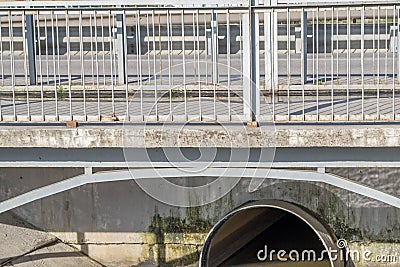 Concrete small bridge with pedestrian path, asphalt road, gray metal fences, with reinforced concrete slab and metal pipe under it Stock Photo