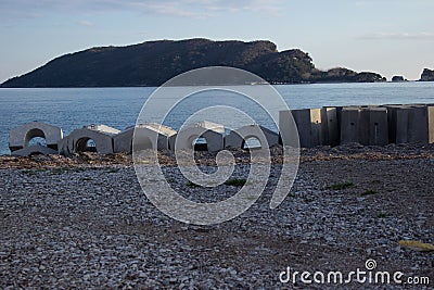 Concrete structures with arched shapes and rectangular blocks are lined up on a pebble beach. Stock Photo