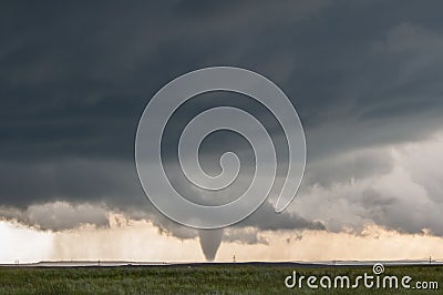 A cone tornado touches down under the base of a dark storm on the plains. Stock Photo