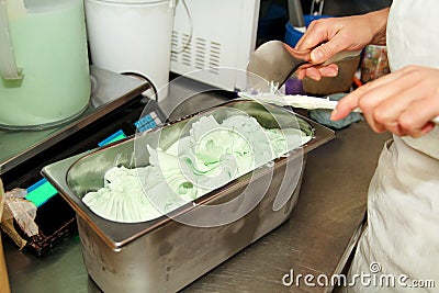 Confectioner in chef uniform is working at ice cream factory. Woman is decorations of italian creamy mint ice cream flavors. Stock Photo