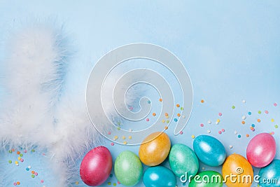 Confetti, bunny ears and colorful Easter eggs on blue table top view. Funny Easter greeting card. Copy space for text. Stock Photo