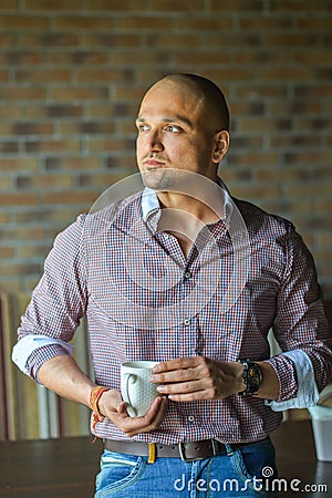 Confidence Indian man standing with cup of coffe and looking at window Stock Photo
