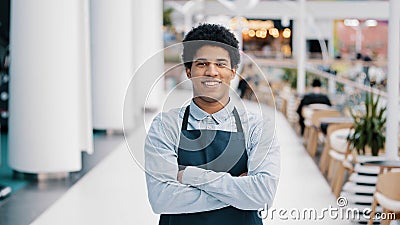Confident African 30s restaurant worker biracial guy strong position standing indoors barman seller waiter in apron Stock Photo