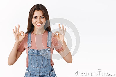 Confident, assertive good-looking woman in denim overalls, t-shirt, showing okay ok approval sign with smile, agree or Stock Photo