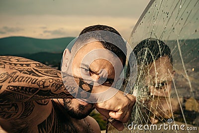 Confident attractive man with serious face cracked glass. Dangerous criminal, hooligan guy on cracked bullet glass. Stock Photo