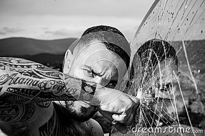 Confident attractive man with serious face cracked glass. Dangerous criminal, hooligan guy on cracked bullet glass. Stock Photo