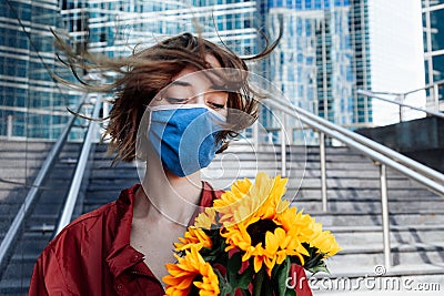 Confident businesswoman in facial mask is awaiting meeting, date, woman with bouquet of sunflowers is standing in financial centre Stock Photo
