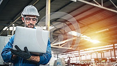 Confident engineer in blue jumpsuit holding laptop computer in a warehouse. Stock Photo