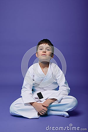 Confident European teenager - aikido fighter - in white kimono sitting in lotus pose while practicing oriental martial arts on Stock Photo