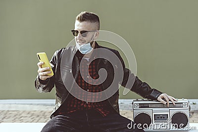 Confident hipster man video calling against green wall background while listening music with a vintage boombox player - Man with Stock Photo