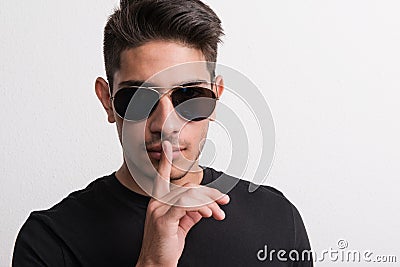 A confident hispanic young man with sunglasses and black T-shirt in a studio. Stock Photo