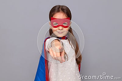 Confident little girl wearing superhero costume and mask isolated over gray background pointing finger to camera choosing you Stock Photo