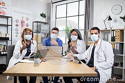 Multiracial doctors in protective masks showing thumbs up at office meeting Stock Photo
