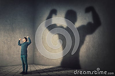 Confident man flexing muscles imagine super power as casting a shadow of muscular bodybuilder showing biceps. Strong person facing Stock Photo