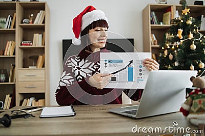 Confident mature adult businesswoman in Santa hat pointing at graphic materials Stock Photo