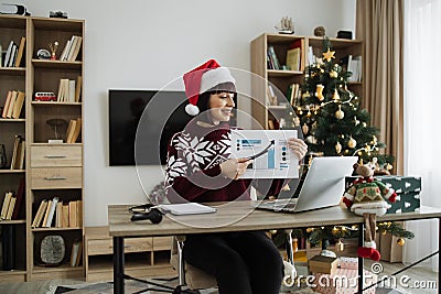 Confident mature adult businesswoman in Santa hat pointing at graphic materials Stock Photo