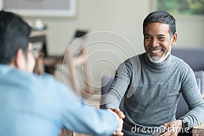 Confident mature Asian man sitting, smiling and shaking hand with partnership after making profitable agreement. Stock Photo